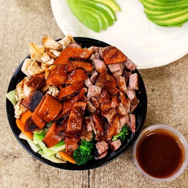 A Best BBQ bowl with chicken, beef, and pork, drizzled with sauce, alongside avocado slices.