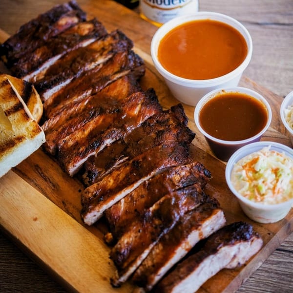 Best BBQ's grilled ribs, coleslaw, and sauces on a wooden board with grilled bread.