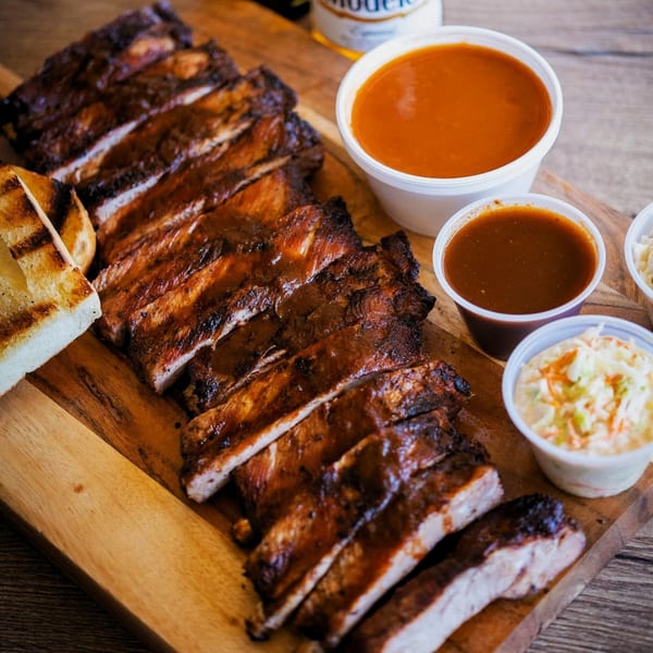 Best BBQ ribs, grilled bread, coleslaw, and two sauces on a wooden board.