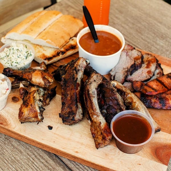 A Best BBQ platter with ribs, chicken, sliced meat, bread, coleslaw, and two cups of BBQ sauce.