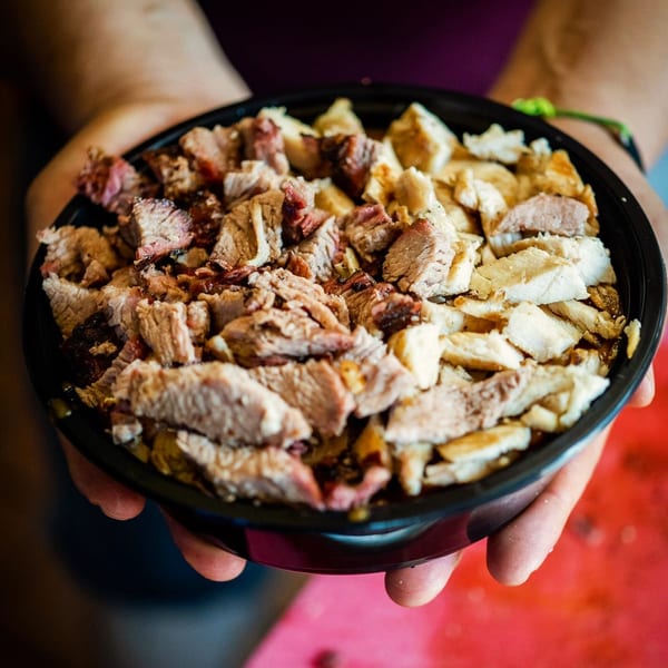 Hands holding a black bowl filled with Best BBQ's chopped brisket and chicken.
